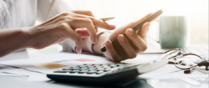 Close-up of a man's hands holding a mobile phone next to a calculator on the table