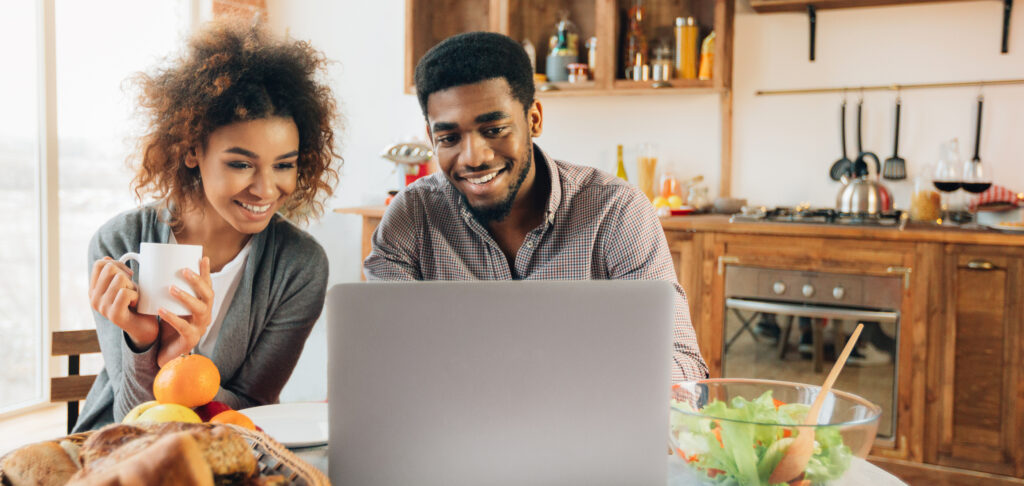 woman looking at her boyfriend working on laptop in kitchen, panorama, copy space