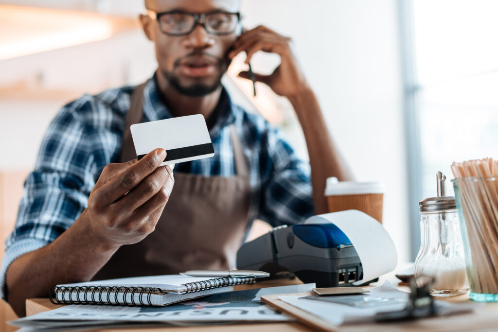 african american male owner working with credit card reader and smartphone in coffee shop