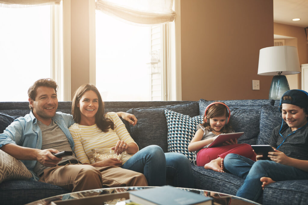 Technology, happy family together and in living room of their home with lens flare.